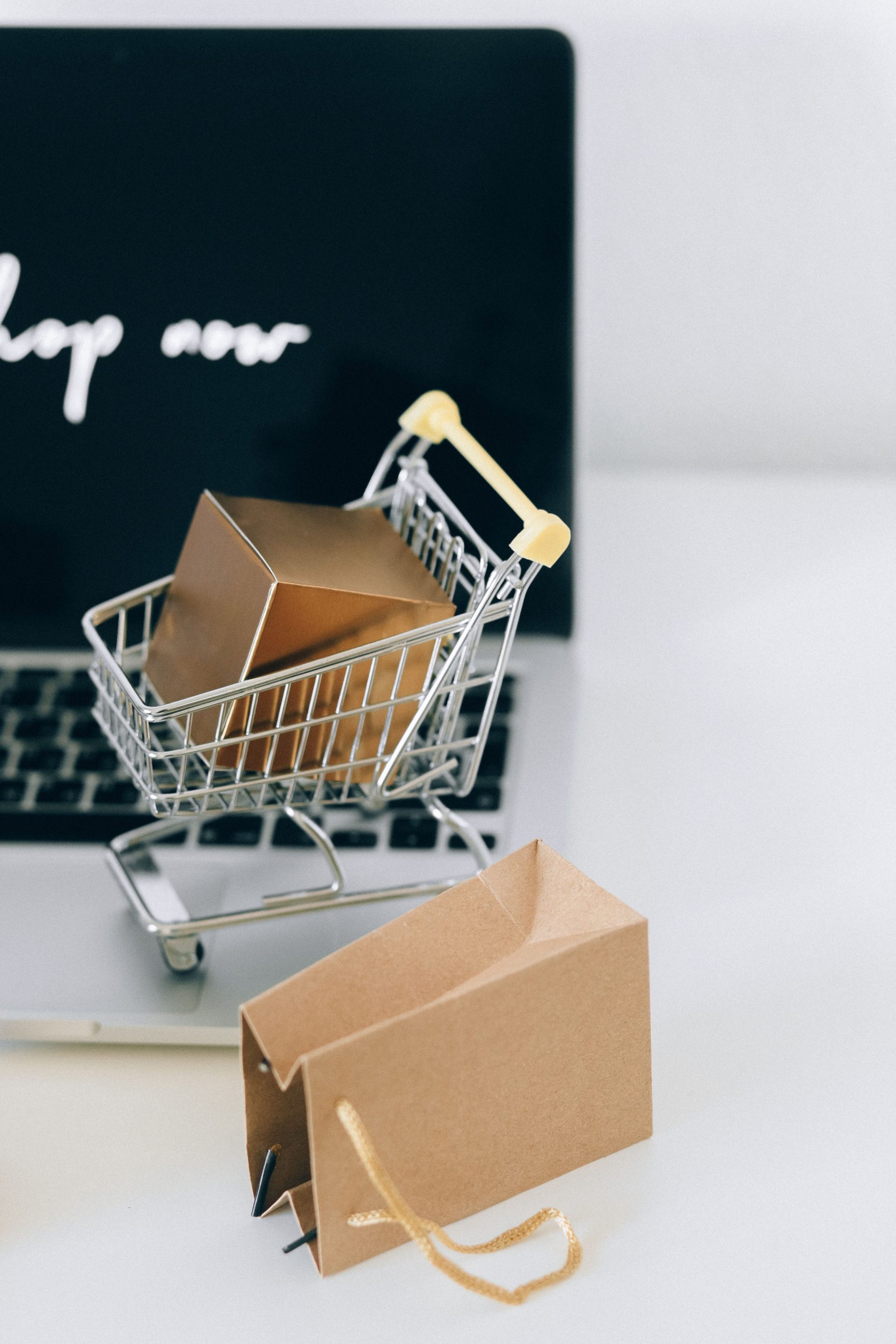 A miniature shopping cart with a parcel on a laptop symbolizes online shopping and e-commerce.